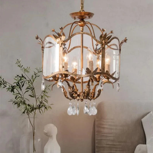 Gold candelabra pendant light with clear crystal droplets hanging from a distressed gold frame and a clear glass shade, illuminating a bedroom setting.