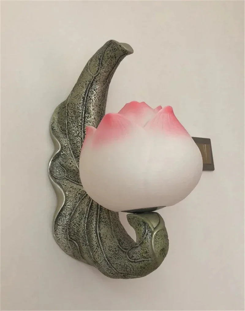 Decorative wall sconce with a leaf design and pink light bulb on a plain background