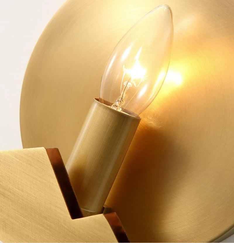 Gold wall sconce with a lit light bulb on a white background