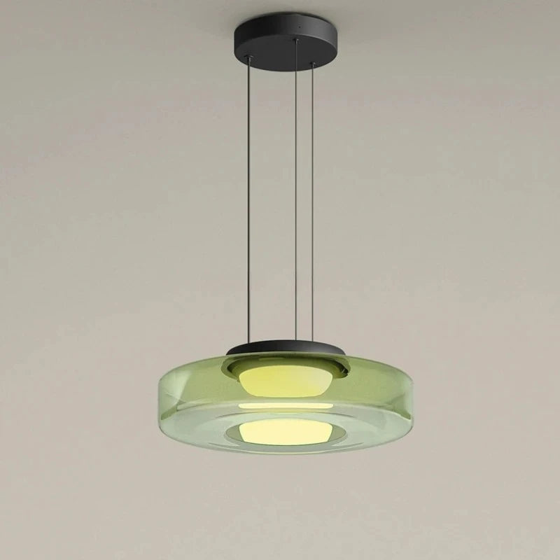 Green glass disk pendant light with a black ceiling mount and cord.