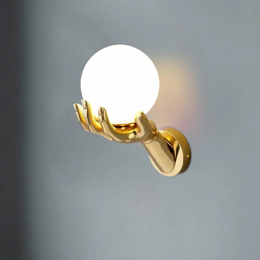 Close-up of a gold hand wall sconce with a lit white globe against a dark gray wall.