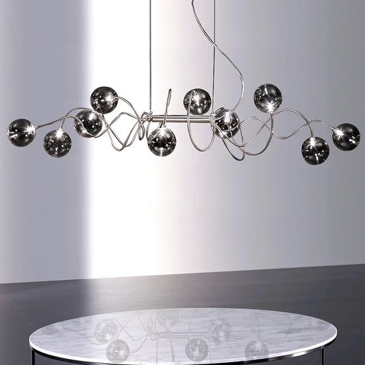 Chrome spiral wave pendant light with multiple smoky gray glass globes reflected in a marble-top table below.