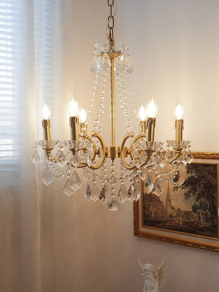 Gold chandelier with crystal accents on a wall with a painting and statue in the background