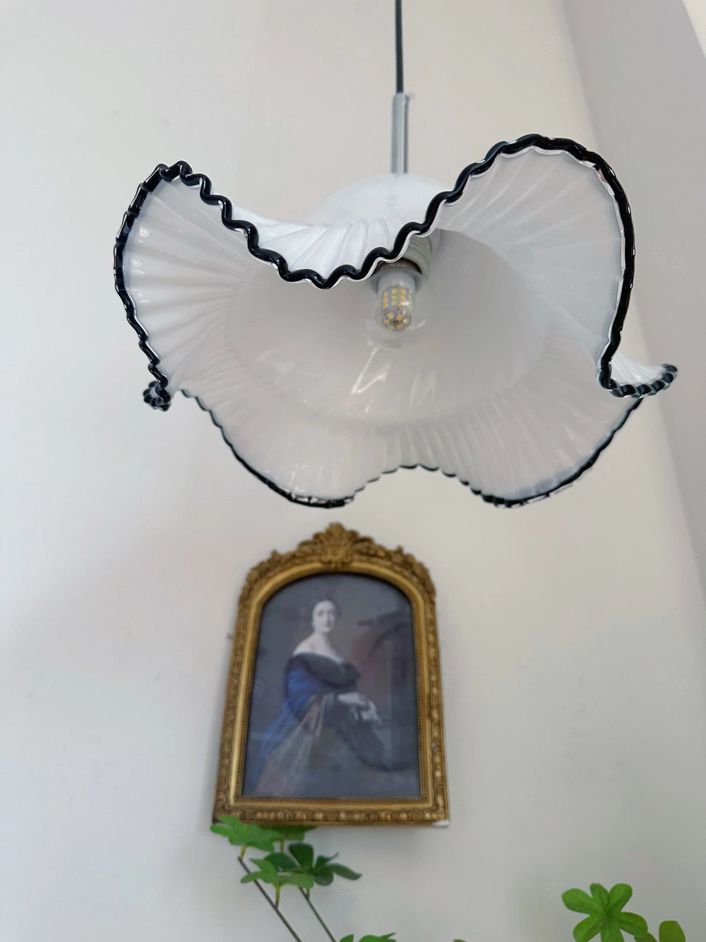 Floral-patterned lampshade with a light bulb inside, hanging above a framed portrait on a white wall.