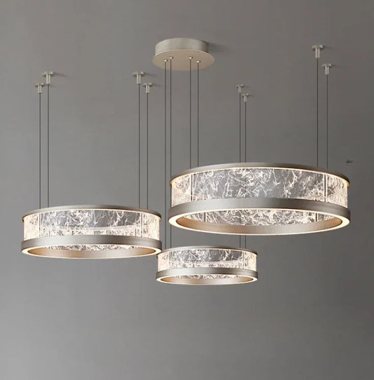 Collection of three ring-shaped pendant lights with textured glass diffusers and silver-toned metal frames, suspended from a grey ceiling.