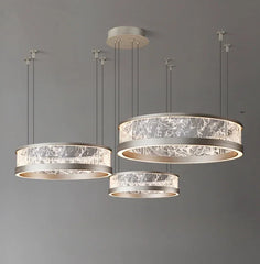 Collection of three ring-shaped pendant lights with textured glass diffusers and silver-toned metal frames, suspended from a grey ceiling.