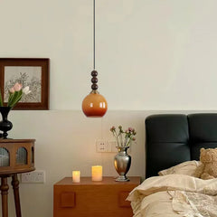 A wood bead and persimmon-shaped globe pendant light hanging above a nightstand with candles and a vase in a bedroom.