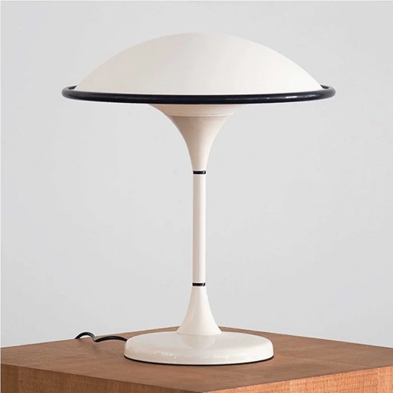 White dome table lamp with a black rim resting on a wooden surface against a white background.