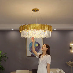 A woman is shown reaching up towards a gold crystal chandelier with a circular frame.