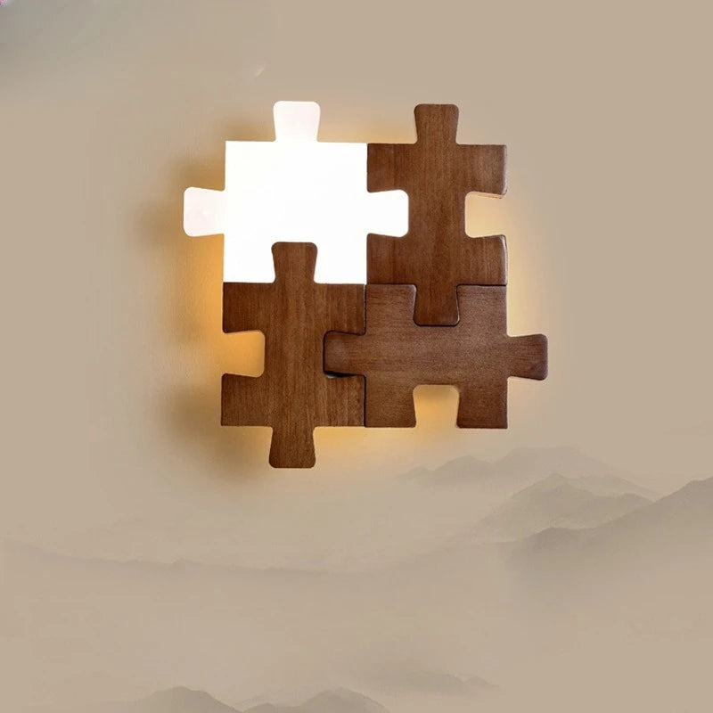 A wooden puzzle-shaped wall sconce with one illuminated white acrylic piece, mounted on a beige wall with a mountainous landscape overlay.