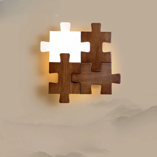 A wooden puzzle-shaped wall sconce with one illuminated white acrylic piece, mounted on a beige wall with a mountainous landscape overlay.