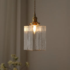 Close-up of a clear glass square pendant light with a brass fixture against a blurred background.