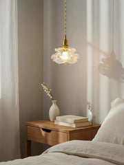 A brass pendant light with a crystal flower shade hanging above a bedside table with books and a vase.