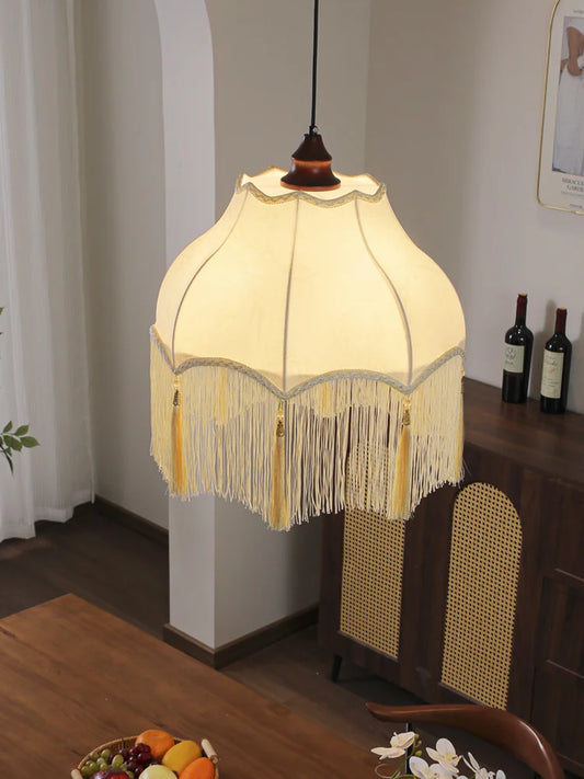 Close-up view of the cream fabric pendant light, highlighting the decorative fringe, gold tassels, and subtle pattern on the shade.