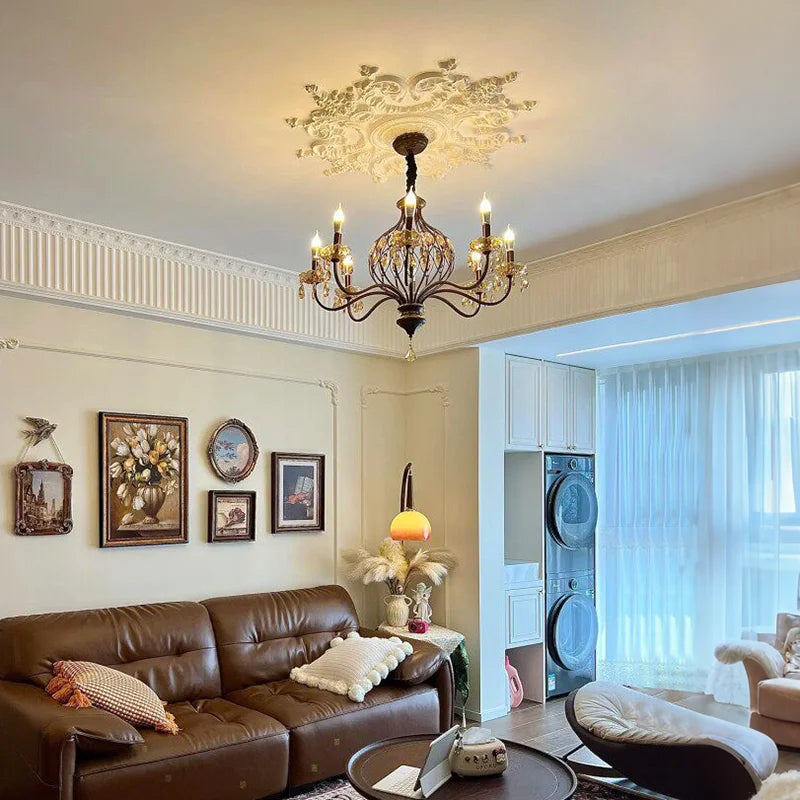 A spacious living room featuring a large brown leather sofa, artwork, and a prominent bronze crystal chandelier hanging from a decorative ceiling.