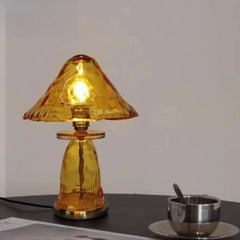 An amber glass mushroom table lamp is illuminated, casting a warm glow on a dark surface.