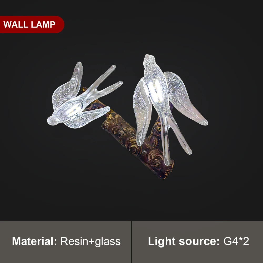 Decorative wall lamp with resin and glass birds on a branch against a black background.