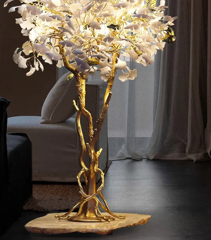 Decorative floor lamp with gold branch-like design and white floral elements in a room setting.