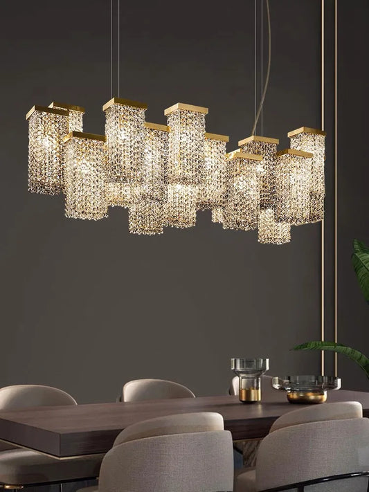 Close-up of a modern gold crystal pendant light fixture featuring multiple rectangular gold tops with cascading crystals, shown above a dining table.