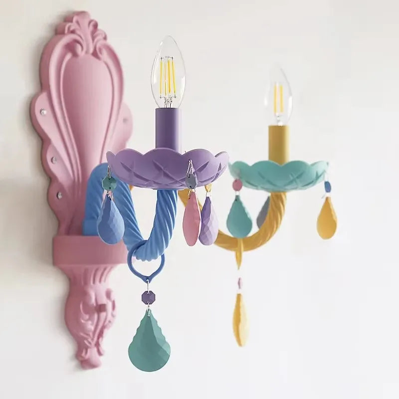 Close-up of a pastel-colored wall sconce featuring floral designs and hanging crystals, with a pink decorative backplate.