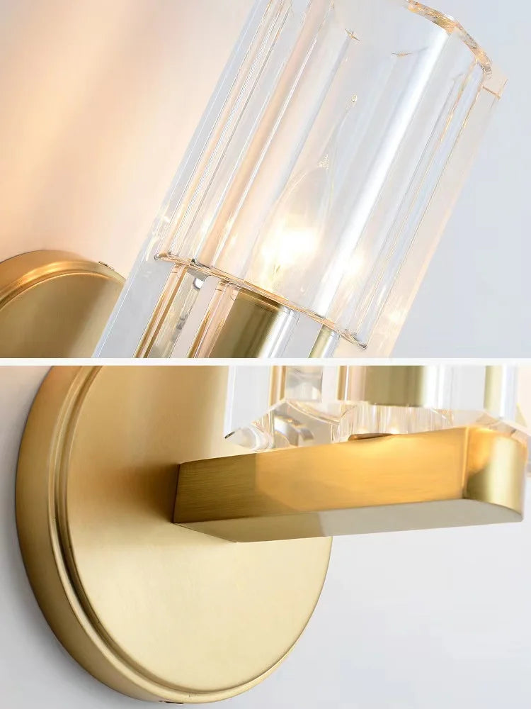Gold wall sconce with clear glass shade on a light gray background