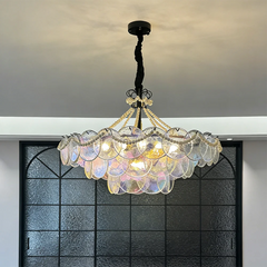 A glass tiered chandelier with pearl accents hanging above a dark window pane background.