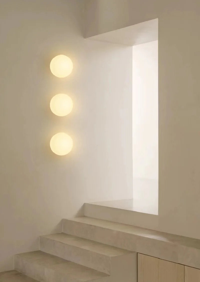 Three round white frosted glass wall lights mounted in a vertical line on a white wall near a staircase and an opening.