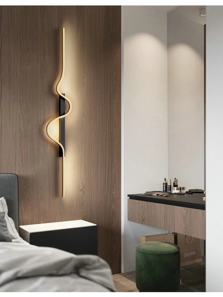 A gold wave wall sconce mounted on a wood-paneled wall next to a bedside table.