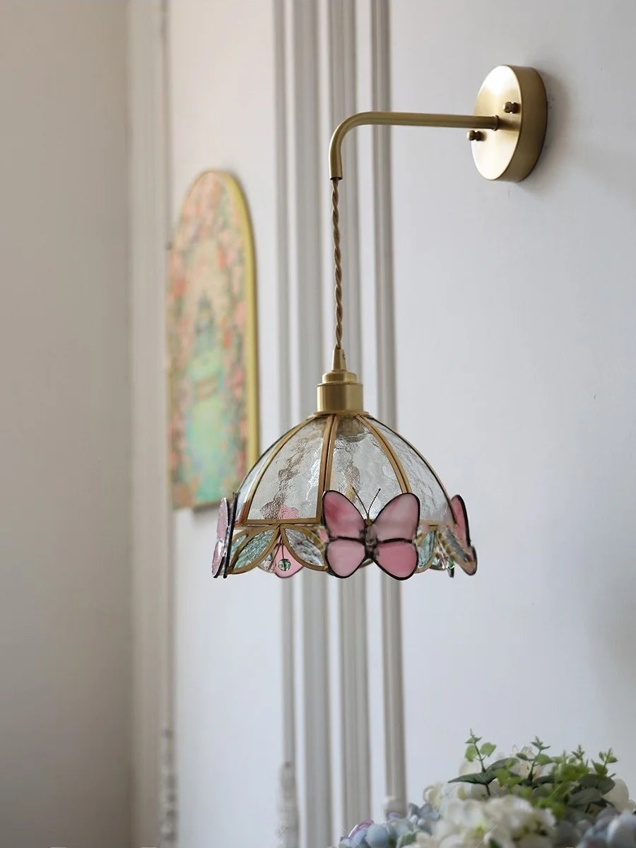 Wall-mounted lamp with butterfly-themed glass shade on a light-colored wall.