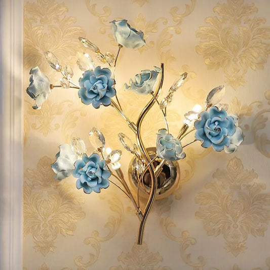 A gold wall sconce with multiple blue floral accents and clear crystal details, mounted on a textured wallpaper.