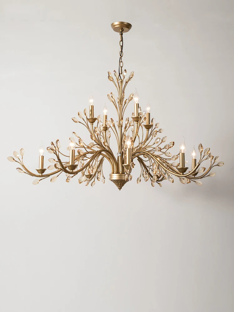 Side view of a brushed gold chandelier with multiple crystal-adorned arms, against a white wall.