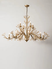 Side view of a brushed gold chandelier with multiple crystal-adorned arms, against a white wall.