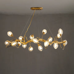 A linear gold chandelier designed to resemble a tree branch with clear, textured glass globes, suspended against a plain dark background.