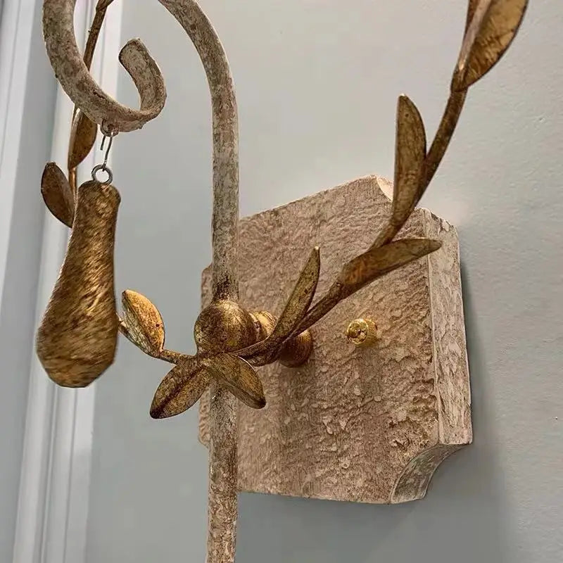 Close-up detail of the distressed gold metal leaf wreath and decorative elements on a wall sconce, mounted on a textured stone-like backplate.
