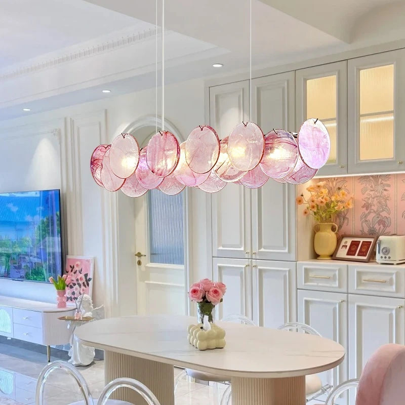 A dining room setting with a long, linear pink crystal chandelier hanging above a modern dining table.
