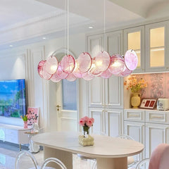 A dining room setting with a long, linear pink crystal chandelier hanging above a modern dining table.