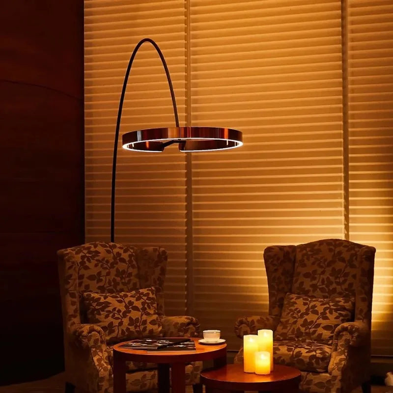 Two patterned armchairs with a small table and floor lamp against a wall with horizontal blinds.