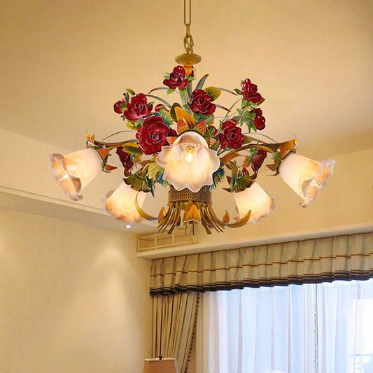 Close-up of a gold floral chandelier with red rose buds and five frosted glass shades, hanging from a ceiling.