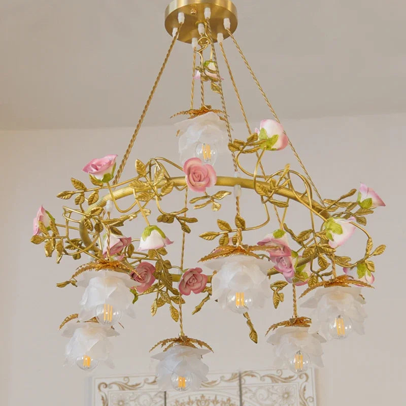 Side view of a gold pendant light adorned with pink ceramic roses and green leaves, with multiple white frosted shades.