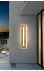 Close-up of a vertical LED wall sconce with a natural stone texture, mounted on a smooth wall next to a glass door.