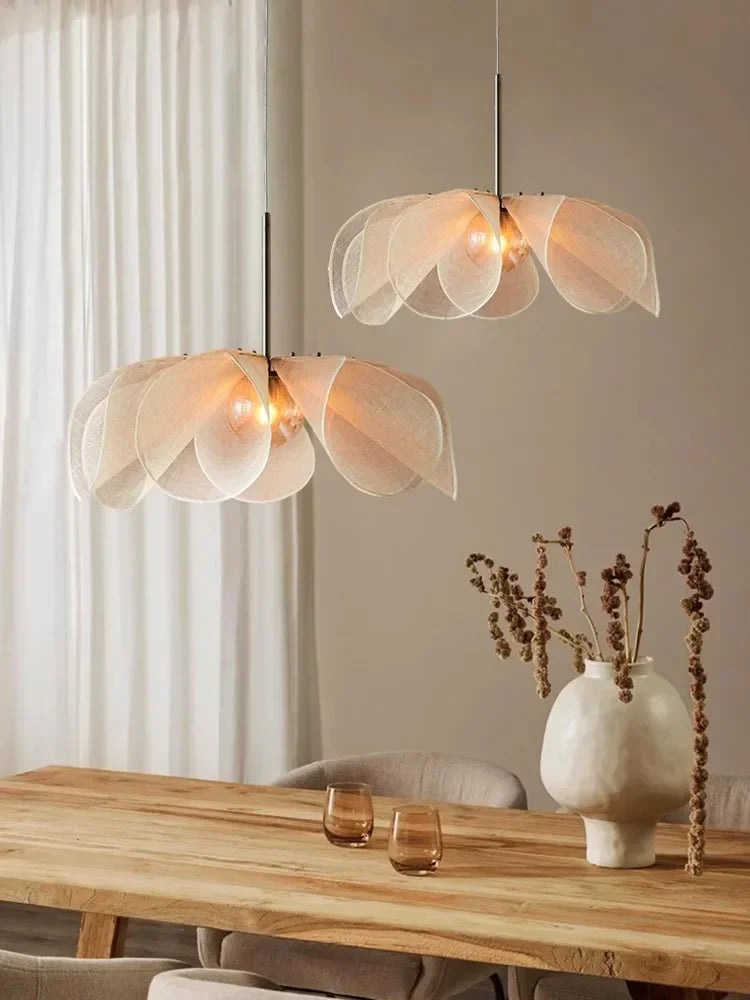 Modern pendant lights hanging above a dining table with a vase and glasses.