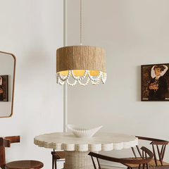 A rattan drum pendant light with a scalloped edge of wooden beads hanging over a round dining table.