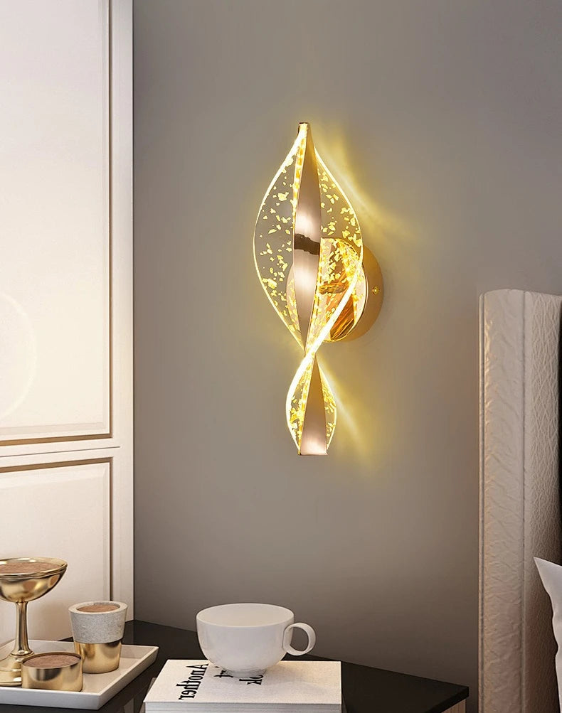 Decorative wall light fixture on a wall with a cup and books on a table below.