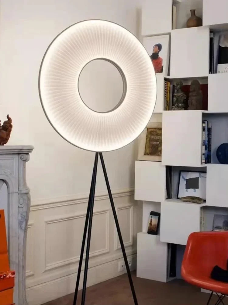 Modern floor lamp with a circular design in a room with a bookshelf and red chair.