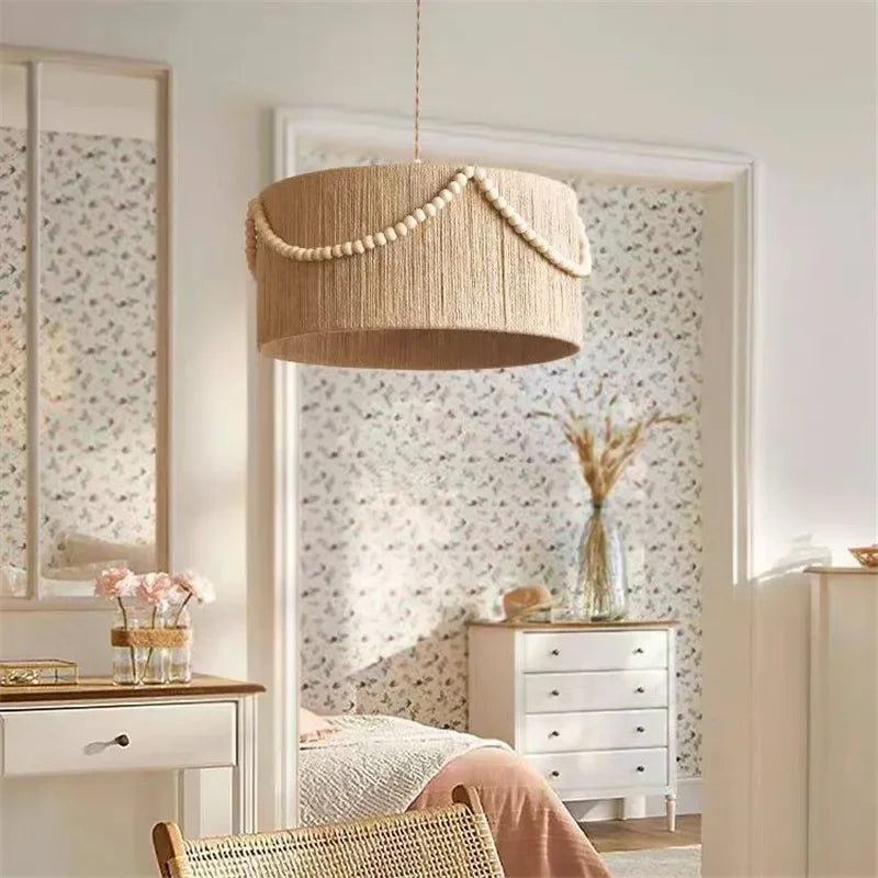 A bohemian-style rattan drum pendant light hangs in a softly lit room with patterned wallpaper and a dresser with flowers.