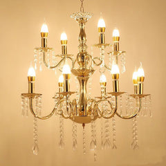 A grand, multi-tiered gold chandelier with candelabra-style arms adorned with cascading clear crystals, illuminated with warm white LED bulbs against a cream background.