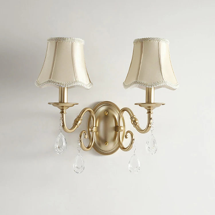 Decorative wall sconce with two cream-colored lampshades and crystal accents on a light gray background.