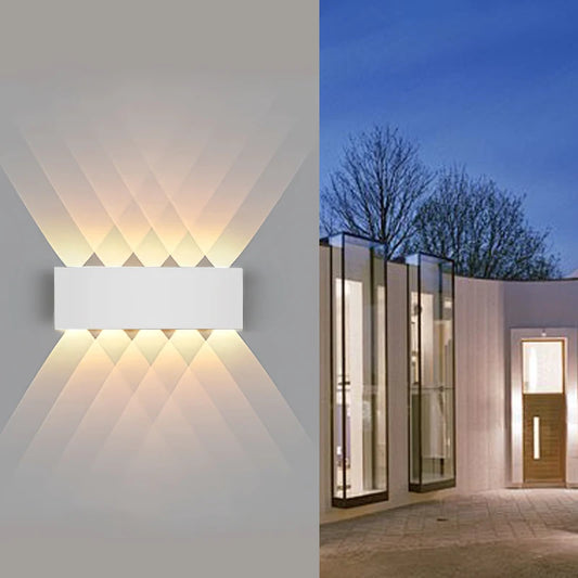 White geometric wall sconce with warm light illuminating a modern exterior facade at dusk.