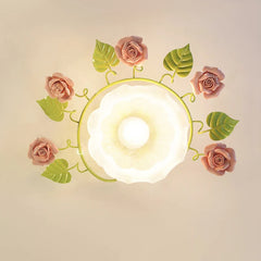 Overhead view of a circular flush mount ceiling light featuring pink ceramic roses and green leaves attached to a light green frame surrounding a frosted white glass diffuser.