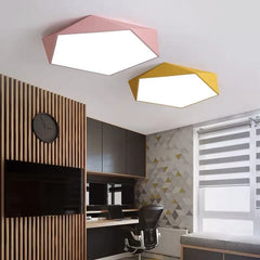 Two modern geometric flush mount ceiling lights in pink and yellow installed in a room with wooden panels.